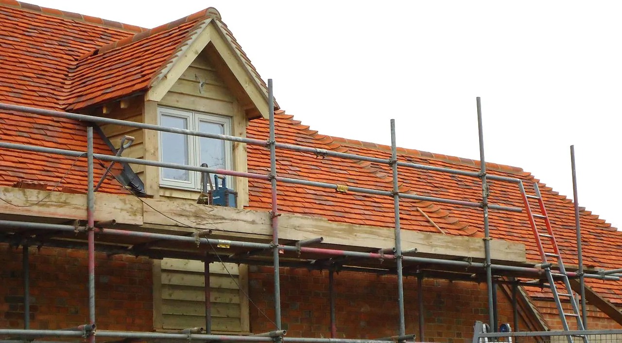 A clay-tiled roof with a timber-clad dormer window, under scaffolding